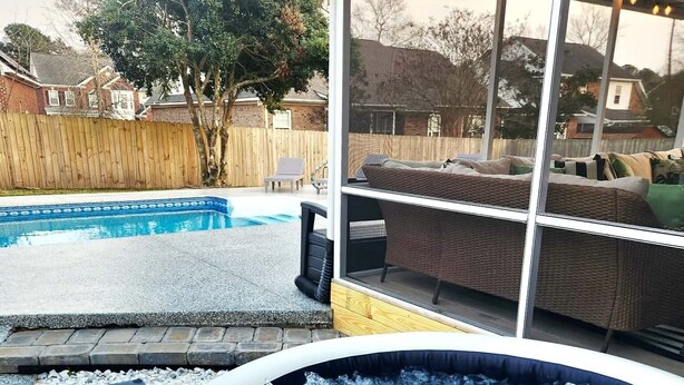 Een hottub met een houten terras en een zwembad op de achtergrond.