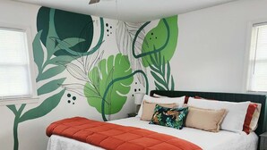 Een slaapkamer met een bed, een plafondventilator, een zebra vloerkleed en een muur met een groen bladmotief.