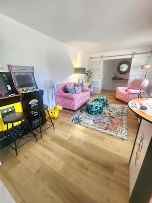 A cozy living room with a pink patterned sofa, a gaming console, a small yellow toy horse, and a colorful rug.