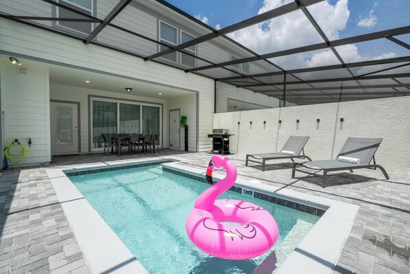 Una piscina con un flotador de flamenco rosa, sillas de descanso y un área de patio techada.