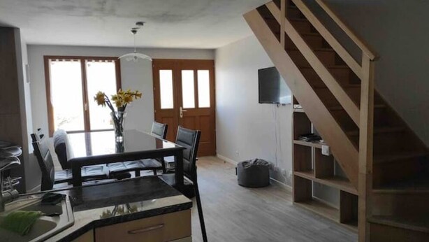 Een moderne keuken met een eettafel, stoelen en een vaas met bloemen. Een trap met een televisie aan de muur.