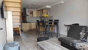 Een compacte woonruimte met een kitchenette, een eethoek met een tafel en stoelen, en een bank.