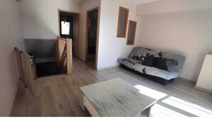Een kamer met een houten vloer, een bank, een tafel en een trap.