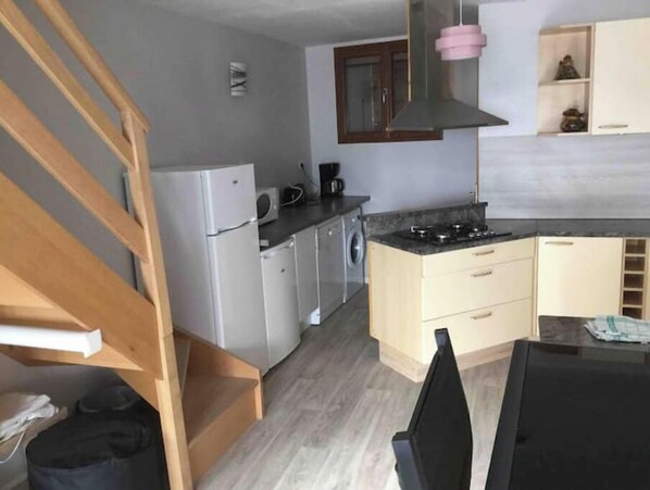 A compact kitchen with a refrigerator, washing machine, and stove.