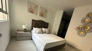 A bedroom with a bed, nightstand, and wall art. - FURNISHED APARTMENT NEAR INTERNATIONAL HOSPITAL FOR RENT RENTAHOSUE (Floridablanca)