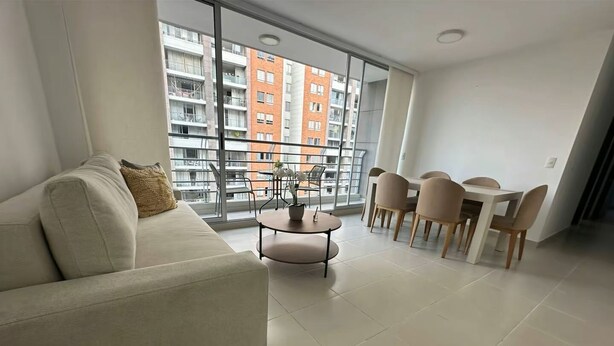 A modern living room with a sofa, a round coffee table, and a dining area with chairs and a table. - FURNISHED APARTMENT NEAR INTERNATIONAL HOSPITAL FOR RENT RENTAHOSUE (Floridablanca)