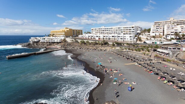 A coastal beach with a rocky shoreline, a pier, and buildings in the background. - Home2Book Apart with Terrace & Pool in Costa Adeje (Adeje)