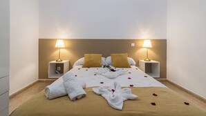 A neatly made bed with rose petals and a towel, two bedside lamps, and a small shelf with a phone. - Home2Book Charming Rooftop Vibes Apartment (Santa María de Guía)