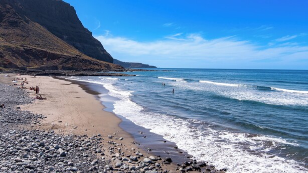 A rocky beach with waves, a clear sky, and a mountain in the background. - Home2Book Charming Rooftop Vibes Apartment (Santa María de Guía)