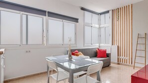 A modern living room with a glass dining table, white chairs, a grey sofa with red cushions, and a wooden slat wall. - Home2Book Charming Rooftop Vibes Apartment (Santa María de Guía)
