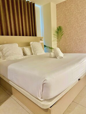 A neatly made bed with white linens, a headboard, and a rolled towel on the side. - Velázquez (Alicante)