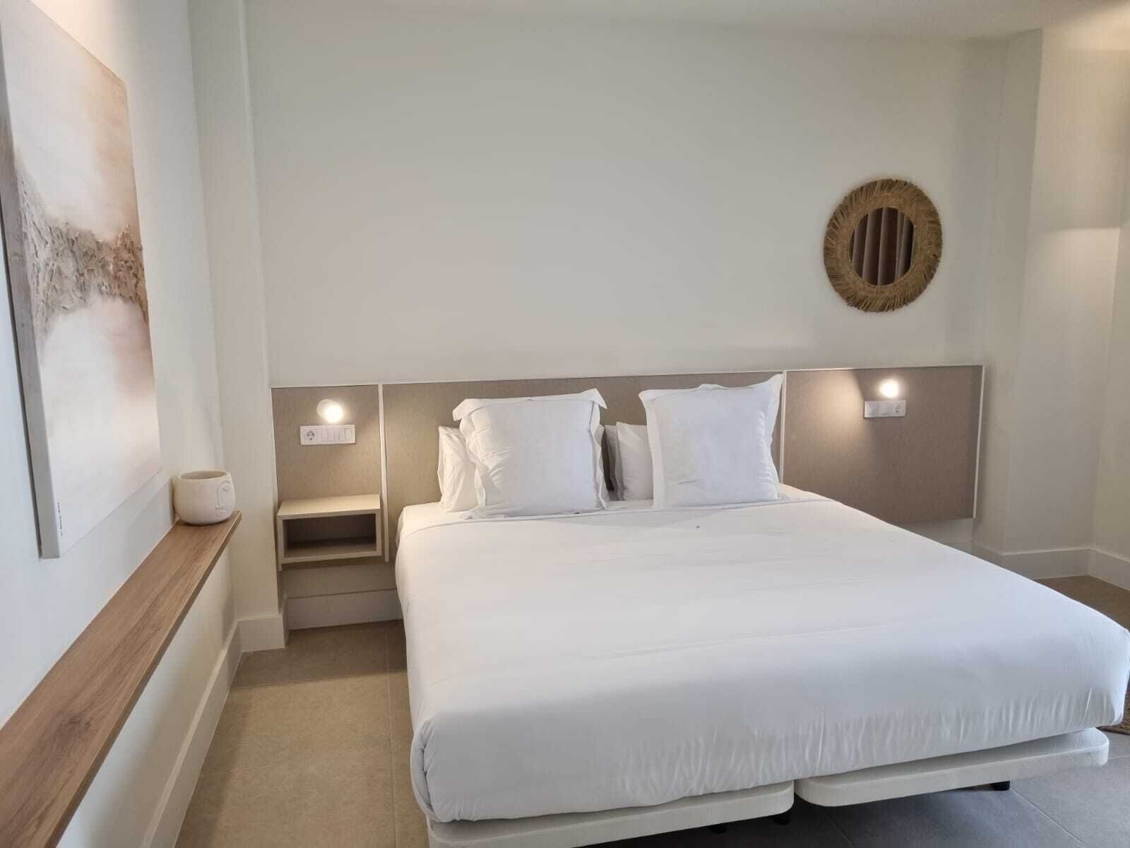 A neatly arranged hotel room with a large bed, a bedside table, a wall-mounted light, and a decorative wall piece.