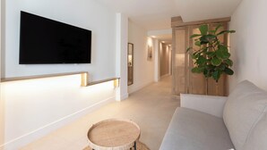 Ein modernes Wohnzimmer mit einem an der Wand befestigten Flachbildfernseher, einem hellen Sofa, einem runden Korbtisch und einer großen Zimmerpflanze.
