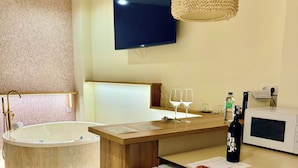 Ein modernes Badezimmer mit einer freistehenden Badewanne, einem Holzausleger mit einer Mikrowelle und einem flachbildfernseher an der Wand.
