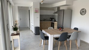 A modern kitchen with wooden cabinets, a grey refrigerator, and a dining area with a wooden table and grey chairs. - Villa Reflets du Sud (LA GAUDE)