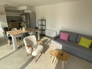 Una sala de estar moderna con comedor, un sofá gris con cojines coloridos, una pequeña mesa de centro de madera y un sillón gris.