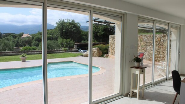 A modern home with a large glass door leading to a swimming pool, surrounded by a stone wall and a view of mountains. - Villa Reflets du Sud (LA GAUDE)