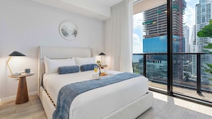 Habitación de hotel moderna con una cama grande, mesitas de noche, vistas de la ciudad y un balcón con una planta.