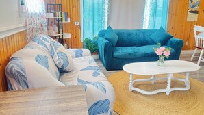 A living room with a blue sofa, a patterned armchair, a white coffee table, and a small plant on the table. - The White Pine Cottage on the Cabot Trail (Englishtown)