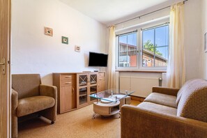 Una sala de estar con un sofá, una mesa de centro de vidrio, un televisor y una ventana con cortinas.
