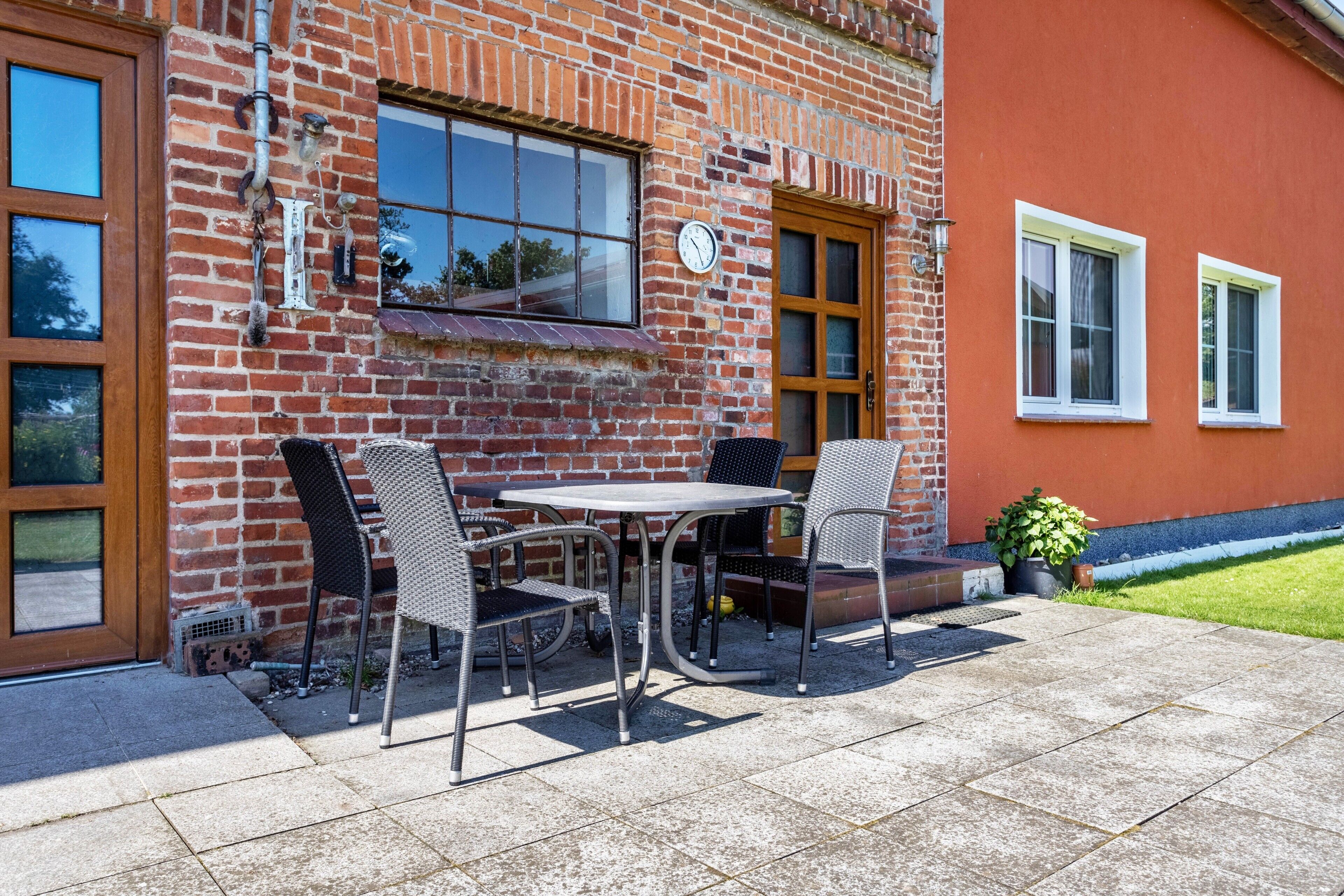 A brick building with a patio area featuring a table and chairs, a clock, and a door.