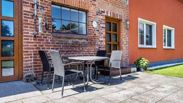 A brick building with a patio area featuring a table and chairs, a clock, and a door.