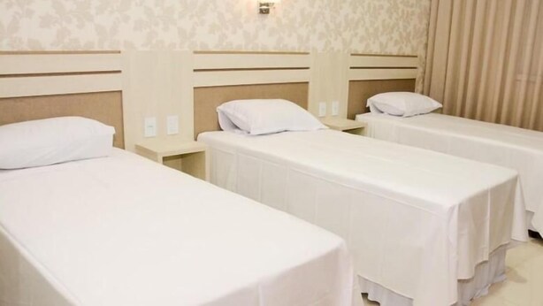A hotel room with three single beds, each with a white bedspread and matching pillows. There is a nightstand with a lamp between the beds, and the walls are decorated with a subtle floral pattern. - Sonus Hotel (Sinop)