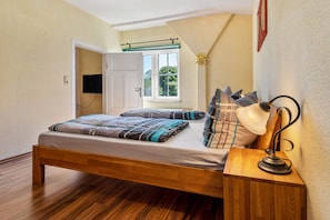 Une chambre à coucher avec un lit en bois, une lampe de chevet, une fenêtre donnant sur un beau paysage et une porte menant à une autre pièce.