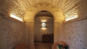 Un pasillo de paredes de piedra con piso de madera, dos sillones de mimbre, una mesita con flores y una cesta de revistas.