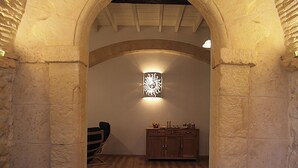 Una habitación con un arco de piedra, suelo de madera, sillas de mimbre y un mueble con objetos decorativos.