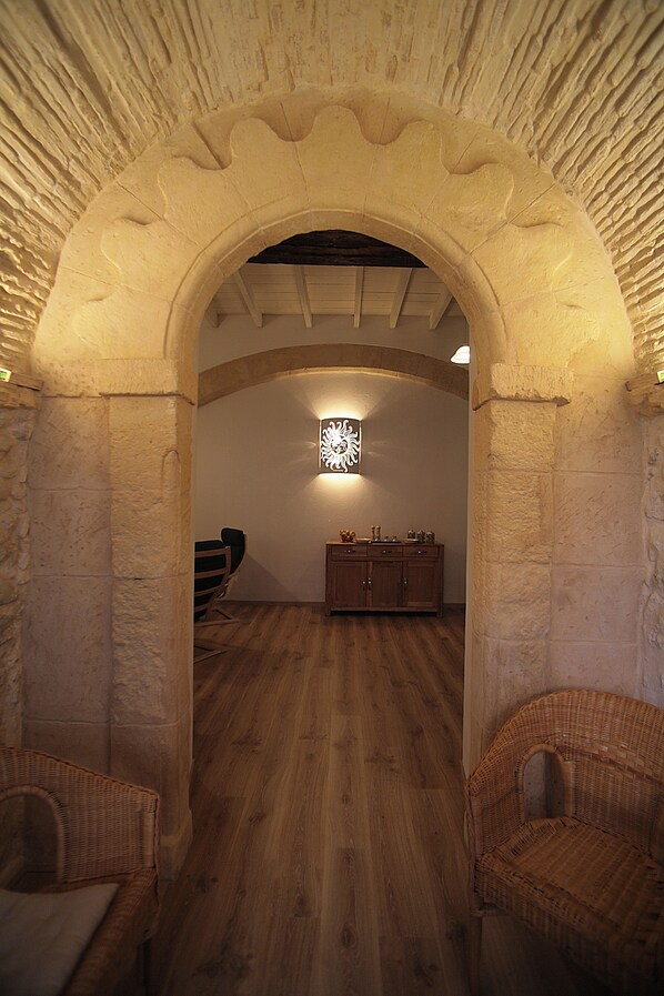 A room with a stone archway, wooden floor, wicker chairs, and a cabinet with decorative items. - "Sun Moon" Historic House San Sperate-South Sardinia (San Sperate)