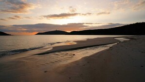 Una playa con una orilla curva, aguas tranquilas y un atardecer al fondo.