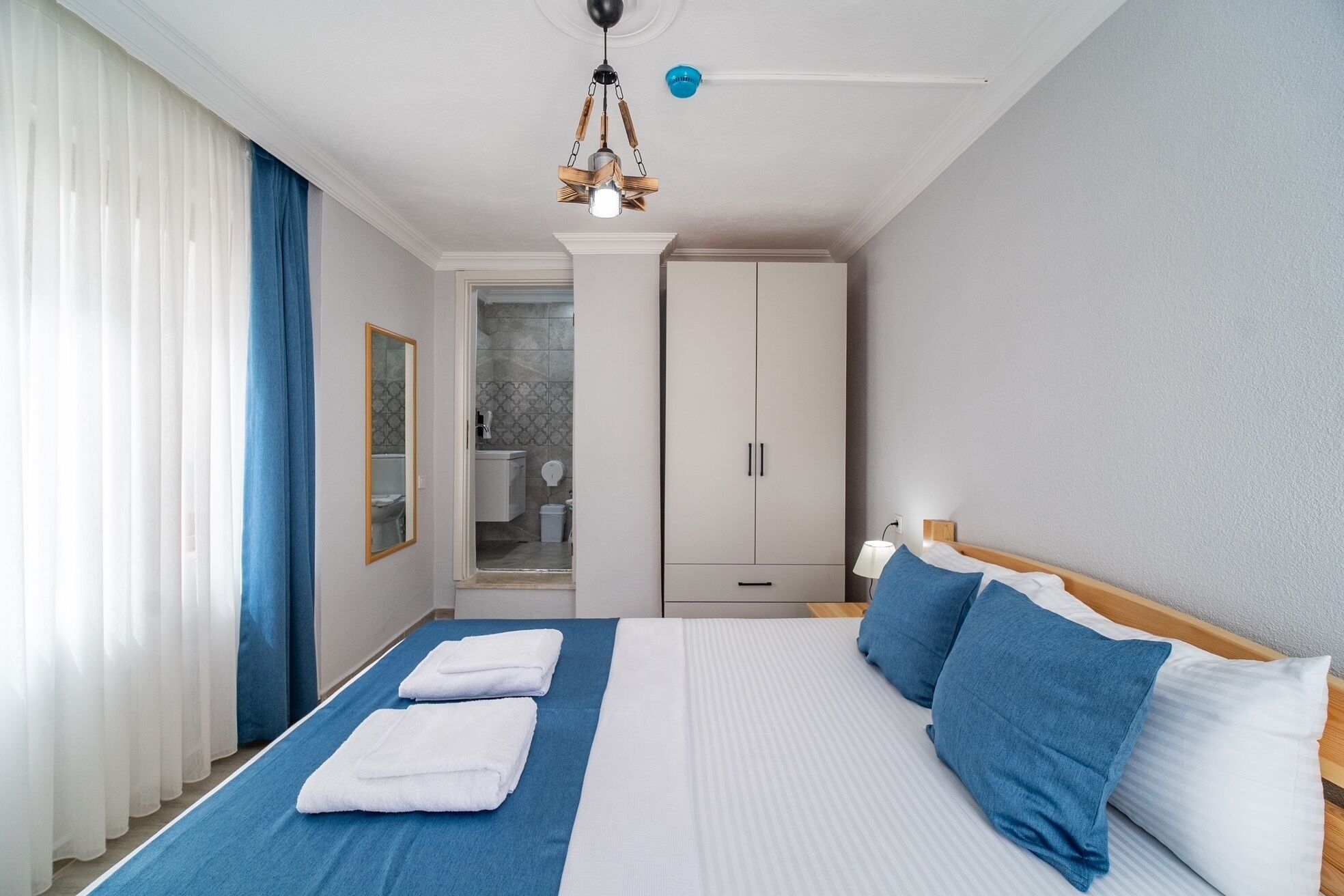 Hotellihuone, jossa on sänky, peili, vaatekaappi ja kylpyhuone, joka näkyy avoimesta ovesta.