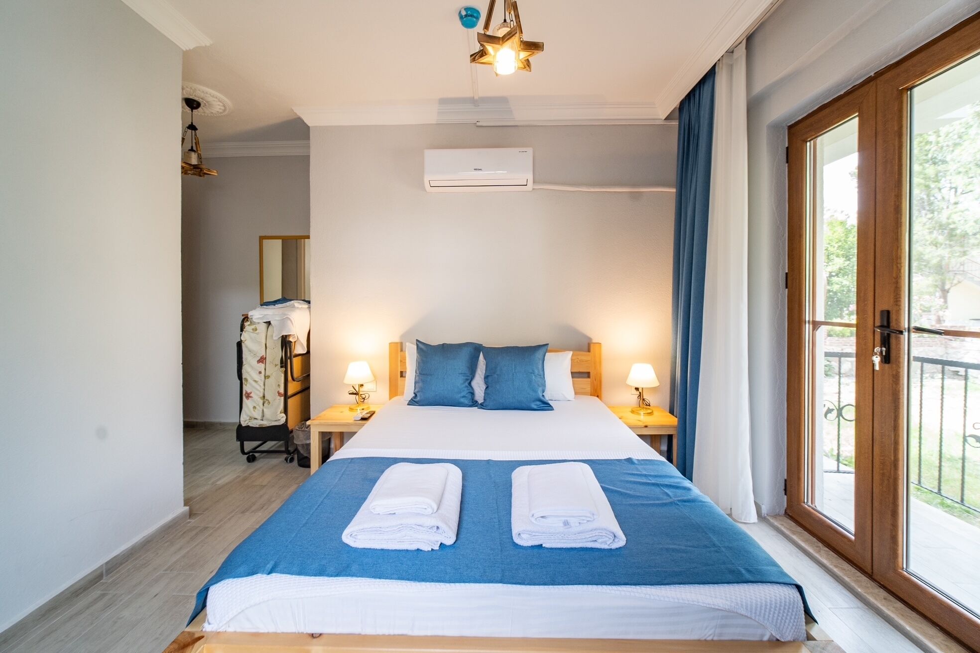 Hotellihuone, jossa on sänky, kaksi yöpöytälamppua, ikkuna verhoilla ja ilmastointilaite.