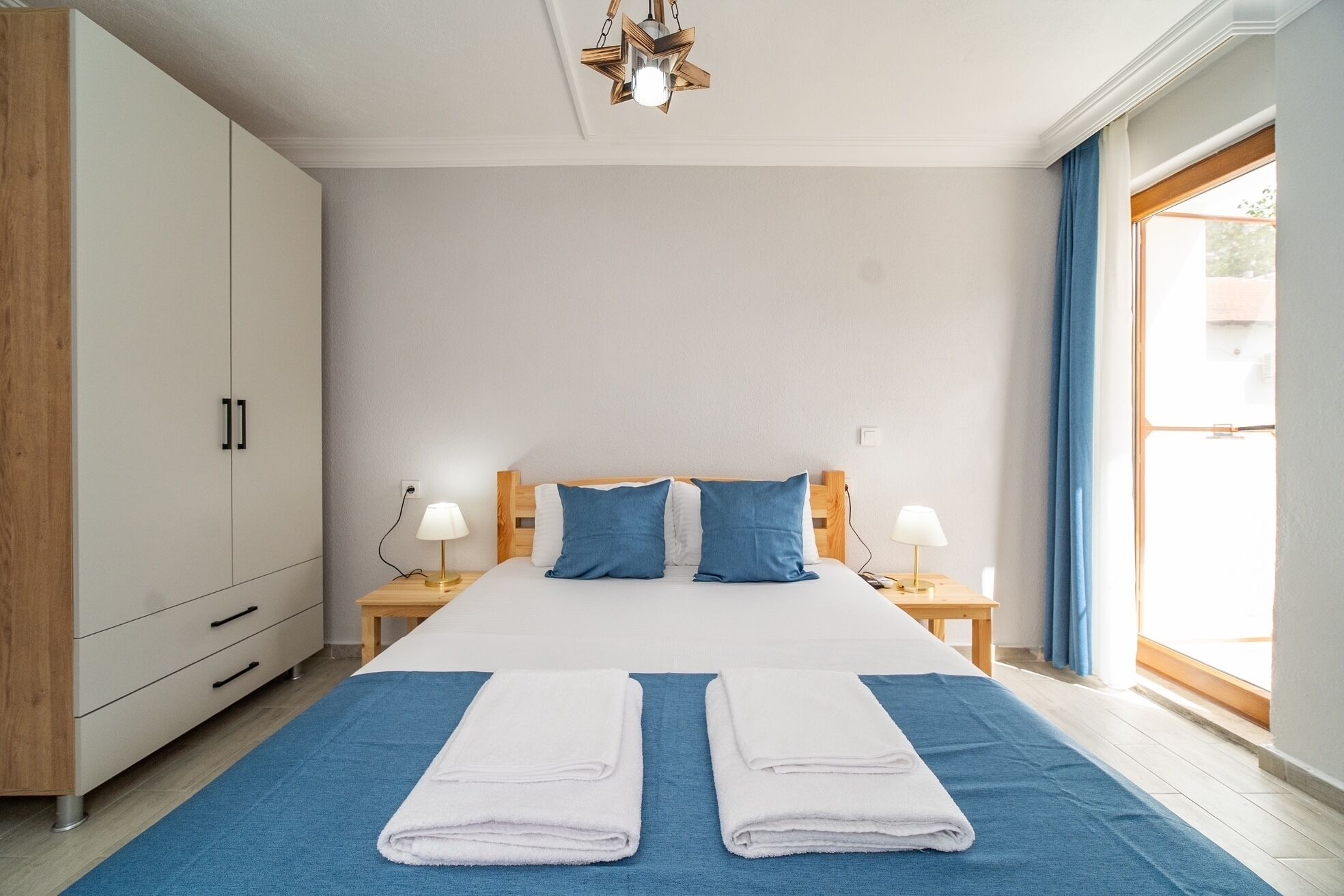 A bedroom with a bed, two nightstands, a wardrobe, and a large window.