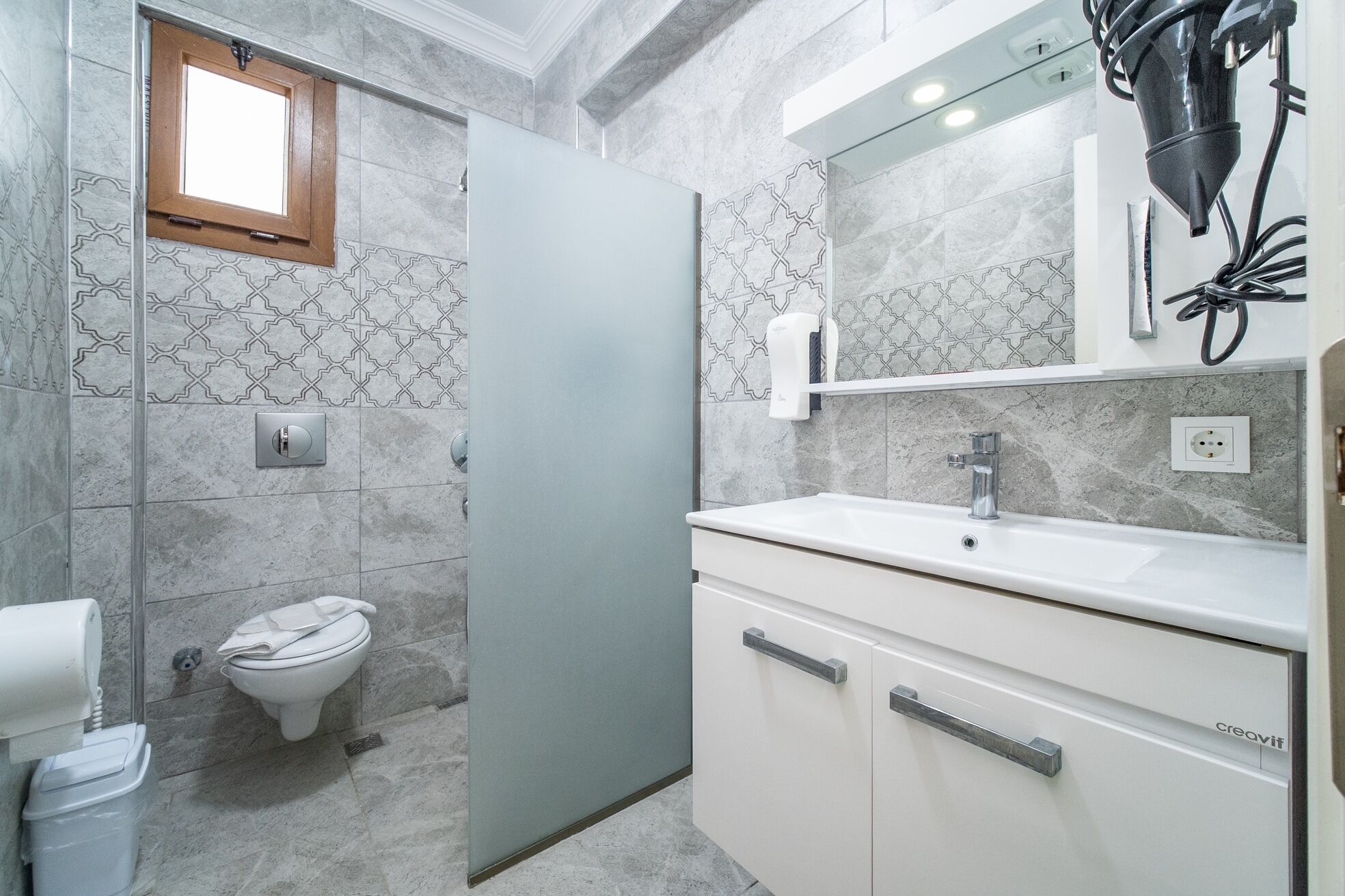A bathroom with a toilet, a sink, a mirror, and a shower area.