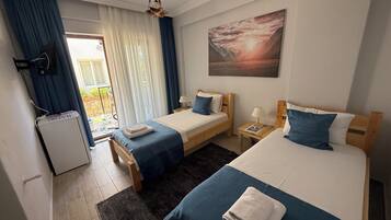 A hotel room with two beds, a heater, a window with curtains, a painting, and a small table with a lamp.