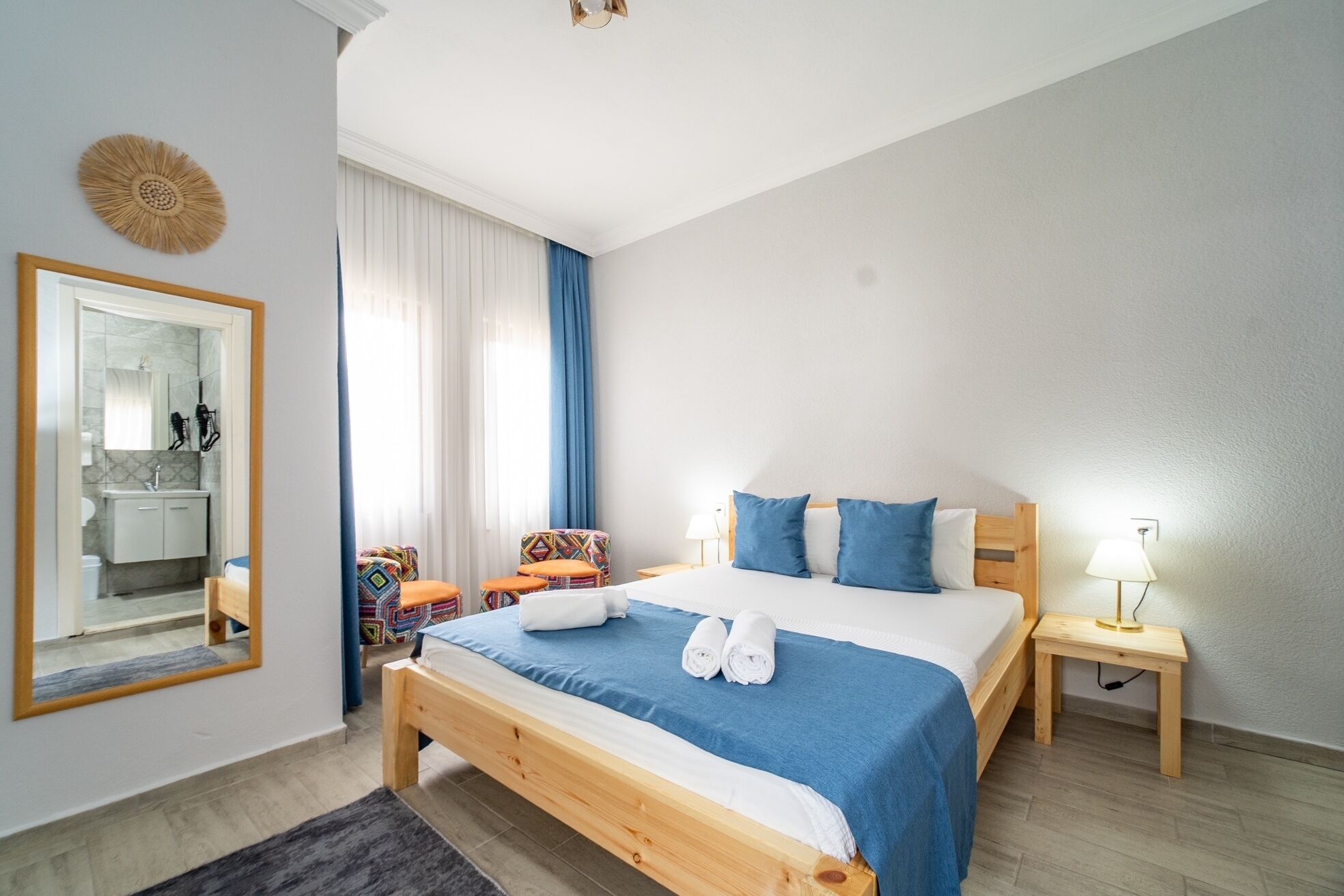 A bedroom with a bed, a nightstand, a lamp, a mirror, and a window with curtains.