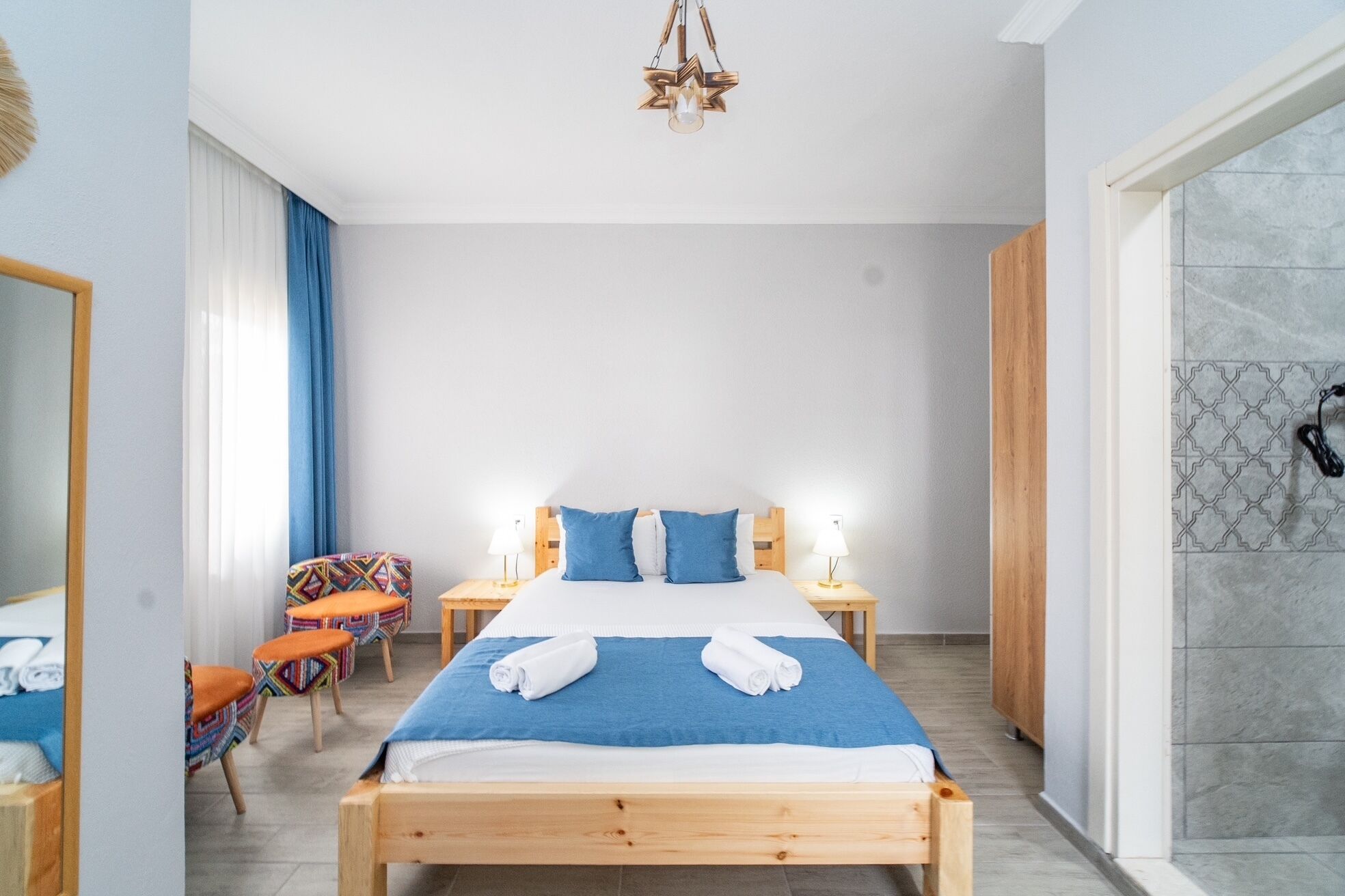 A hotel room with a wooden bed, two bedside tables with lamps, a chair, and a shower area.