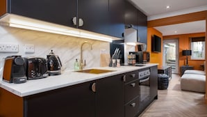 Une cuisine moderne avec des meubles de couleur sombre, un plan de travail en marbre, un robinet doré et un four encastré.