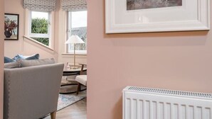 A modern living room with a grey sofa, a white radiator, and a framed abstract painting on the wall. - The Nevis Suite at Munro Guest House (Stirling)