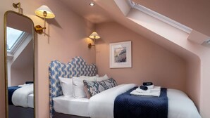 A bedroom with a sloped ceiling, a large mirror, a bed with patterned headboard, and wall-mounted lamps. - The Nevis Suite at Munro Guest House (Stirling)