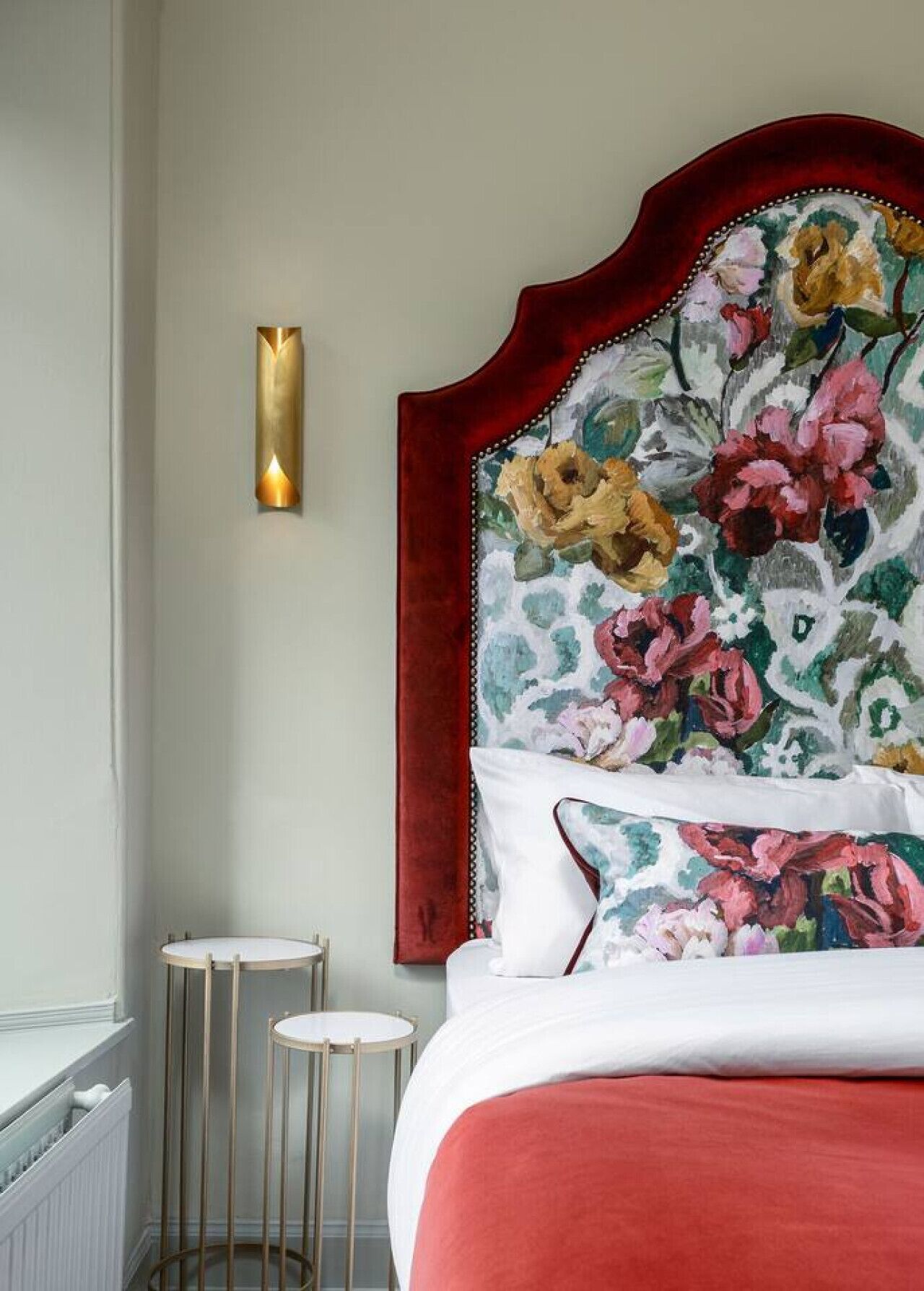 A bedroom with a floral headboard, a bedside table, and a wall-mounted light fixture.