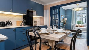 A modern kitchen with blue cabinets, a marble countertop, and a dining area with a wooden table and chairs.