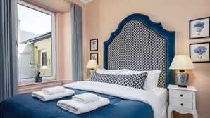 Una habitación de hotel con una cama grande, dos mesitas de noche, una ventana con cortinas y cuadros en la pared.