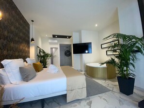 Une chambre d’hôtel moderne avec un grand lit, une télévision, une salle de bain et une plante en pot.