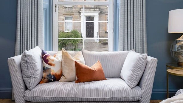 A room with a striped sofa, a patterned rug, and a view of a building through a window with curtains.