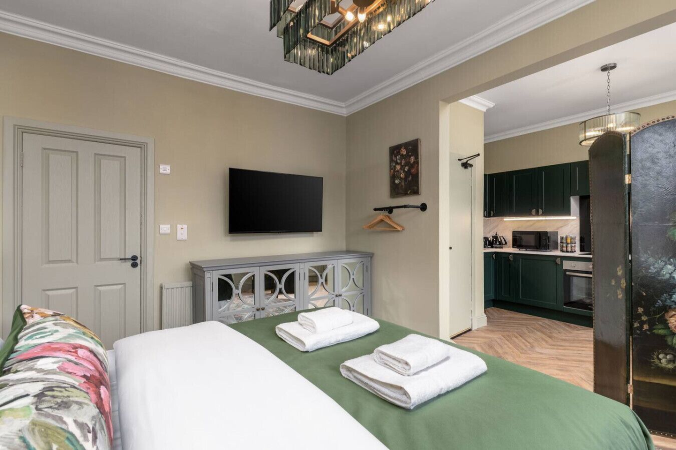 Ein Hotelzimmer mit Bett, Fernseher, einer kleinen Ablage und Blick zur Küche.