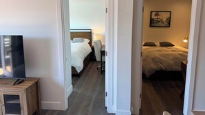 A hotel room with a bed, a desk with a chair, a television, and a painting on the wall. - Cozy 2-Bedroom Guesthouse with Private Patio (San Francisco)