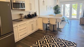 A modern kitchen with white cabinets, stainless steel appliances, and a dining area with a table and chairs. - Cozy 2-Bedroom Guesthouse with Private Patio (San Francisco)